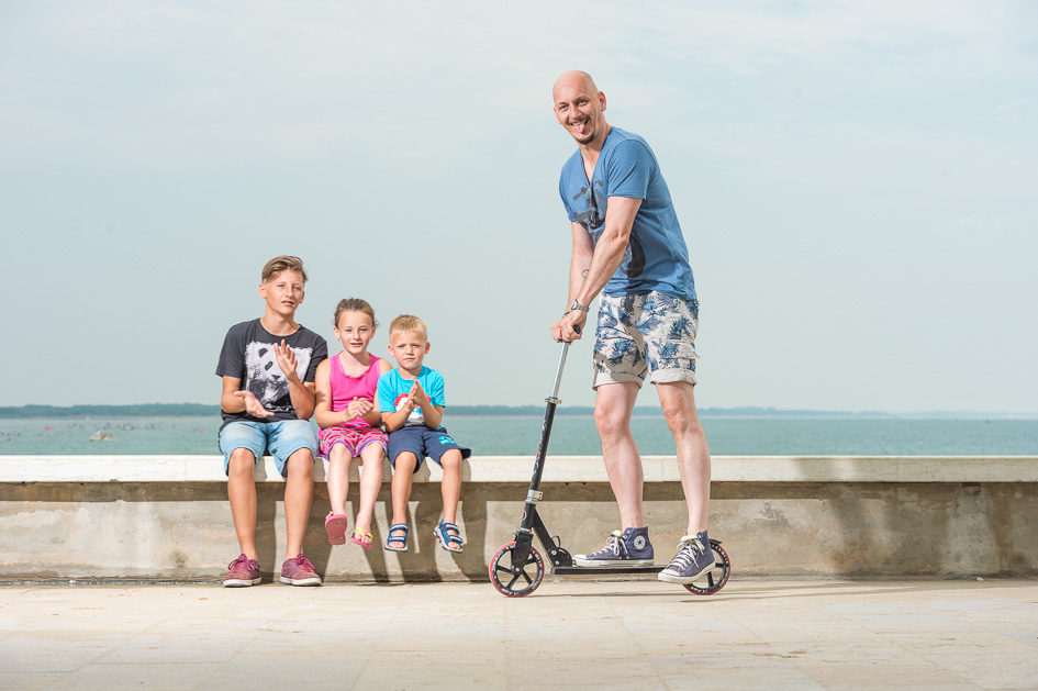 Fröhliches Familienfoto am Meer – Vater mit seinen drei Kindern beim sommerlichen Outdoor-Fotoshooting mit Hannes Pacheiner