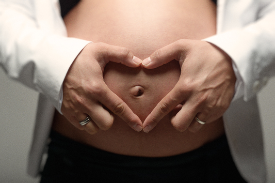 Hände formen ein Herz vor dem Babybauch, Nahaufnahme im Studio