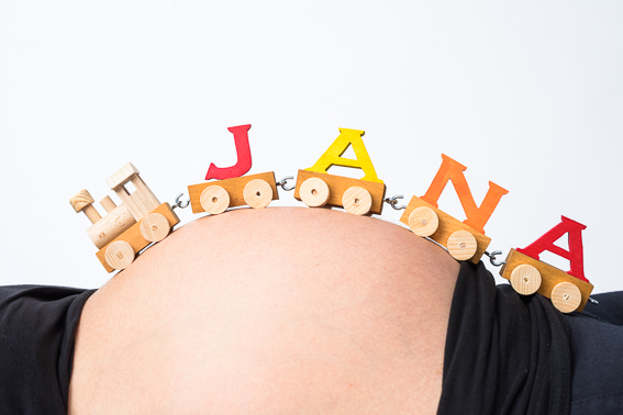 Babybauch mit kleinem Holz-Zug und bunten Buchstaben oben auf dem Bauch im Studio