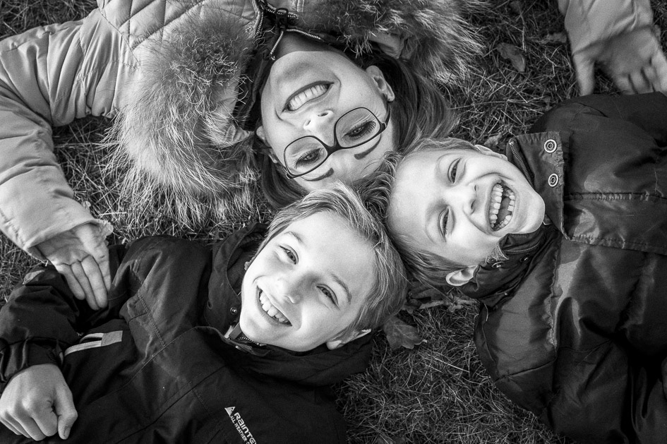 Herzliches Familienfoto in Schwarzweiß – Mutter und zwei Kinder liegen lachend im Gras, aufgenommen von Hannes Pacheiner, Familienfotograf in Villach