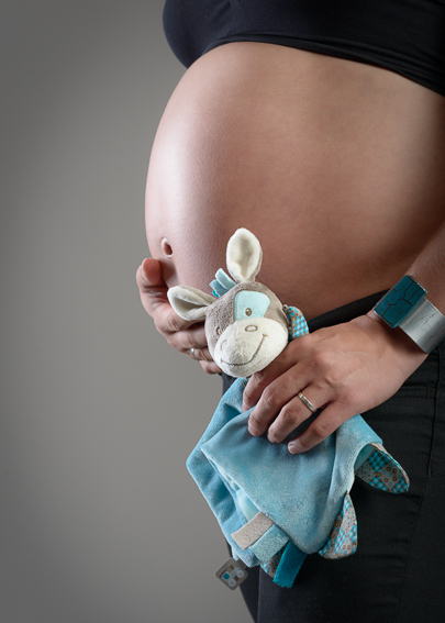 Babybauch in Nahaufnahme, eine Hand hält ein kleines Stofftier als Detail im Studio