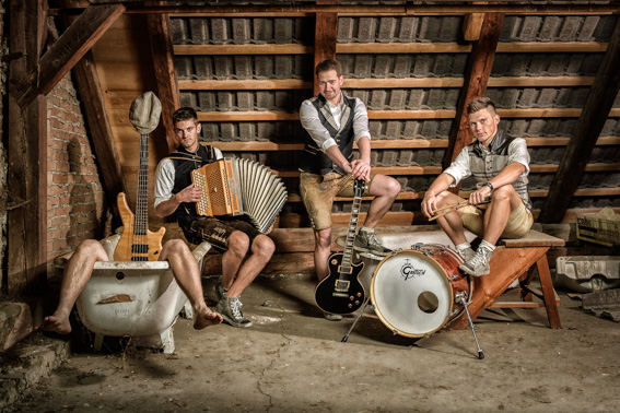Musikgruppe in rustikaler Umgebung mit Instrumenten, inszeniertes Gruppenportrait mit Fokus auf Persönlichkeit und Zusammenhalt