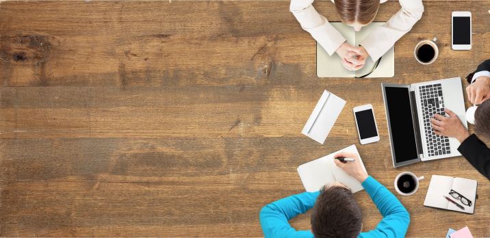 Drei Personen sitzen an einem Holztisch und diskutieren über Content wie Texte, Videos, Podcast oder Whitepaper