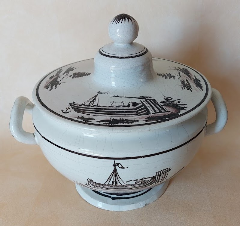 Soupière - Haut. 27 Diam 24 : le décor essentiellement limité aux bateaux (besognes de Seine) est réalisé en camaïeu manganèse. La forme des anses détachées est caractéristique.