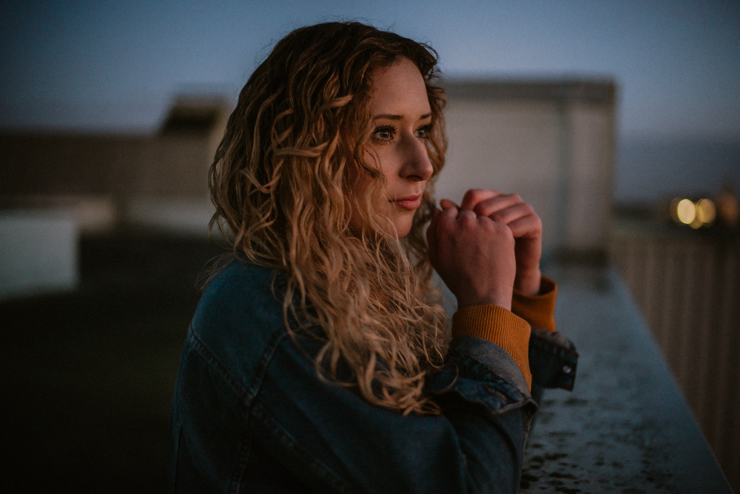 Frau mit Jeansjacke und Locken schaut gedankenvoll in die Ferne