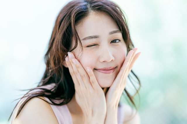 頬に手をあててにっこり微笑む女性｜小顔整体後、リラックスした表情で顔のゆがみが整い、自然な笑顔を見せる女性。優しい矯正でリラックスした状態に。