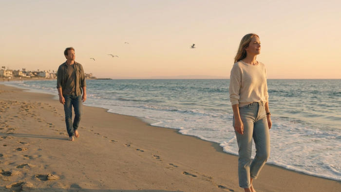 Un uomo e una donna camminano sulla spiaggia al tramonto, a breve distanza l’uno dall’altra, simbolo di libertà personale e fiducia nella relazione.