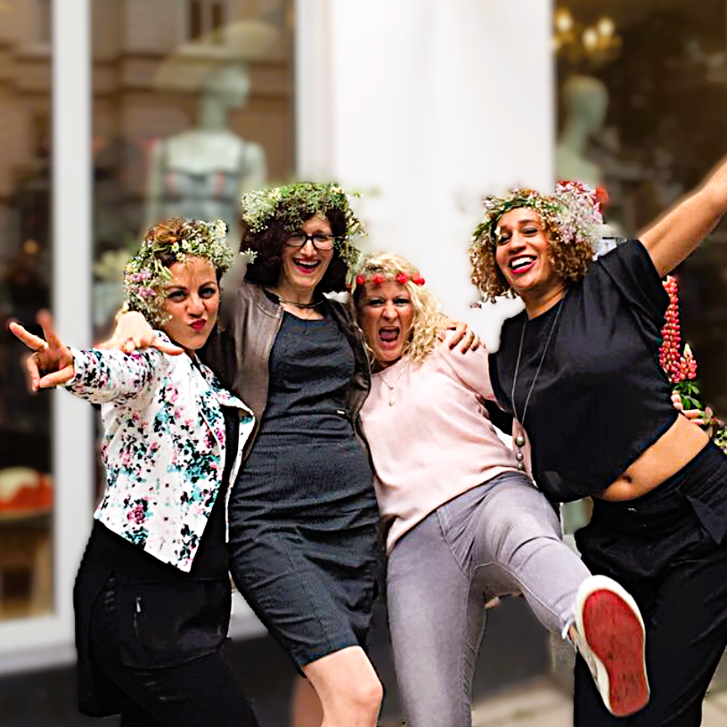Vier Frauen mit Blumenkränzen feiern ausgelassen eine Dessous-Party. Sie lachen, jubeln und haben die Arme umeinander gelegt. Fröhliche Stimmung vor dem Dessousgeschäft DESSOUSTERI in Hamburg