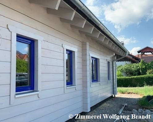 Holzhaus in massiver Blockbauweise  mit 275 mm dicken Blockbalken -  Fenster mit blauen Fensterrahmen  - Diffusionsfähiger Außenanstrich in Cremeweiß