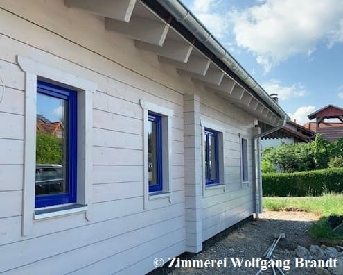 Holzhaus in massiver Blockbauweise  mit 275 mm dicken Blockbalken -  Fenster mit blauen Fensterrahmen  - Diffusionsfähiger Außenanstrich in Cremeweiß 
