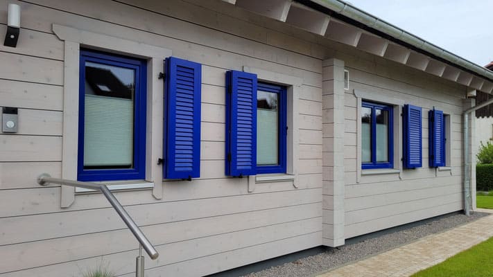 Ebenerdiges Holzhaus in massiver Blockbauweise mit blauen Klappläden 