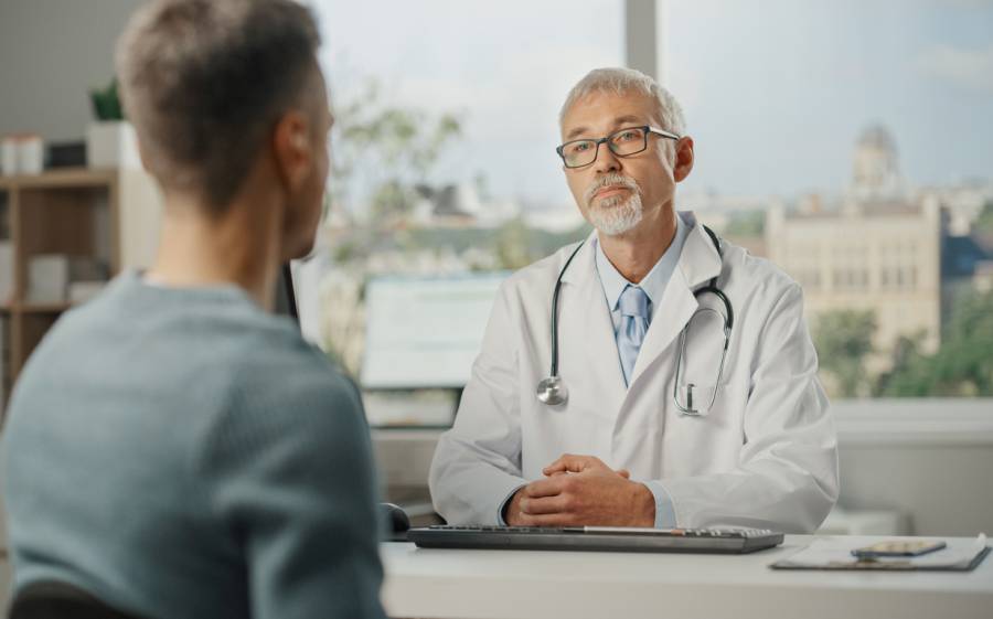 Ein Hausarzt spricht in seinem Behandlungszimmer mit einem jungen männlichen Patienten. (Foto: iStock/gorodenkoff)