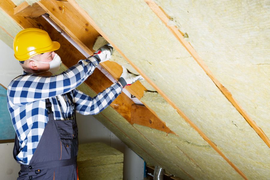 Ein Mann dämmt ein Dach mit Mineralwolle-Platten. (Foto: iStock/artursfoto)