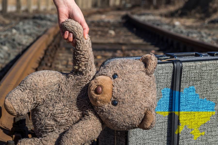 Eine Kinderhand hält neben einem Koffer einen Teddybären an der Hand (Symbolbild: iStock/Animaflora)