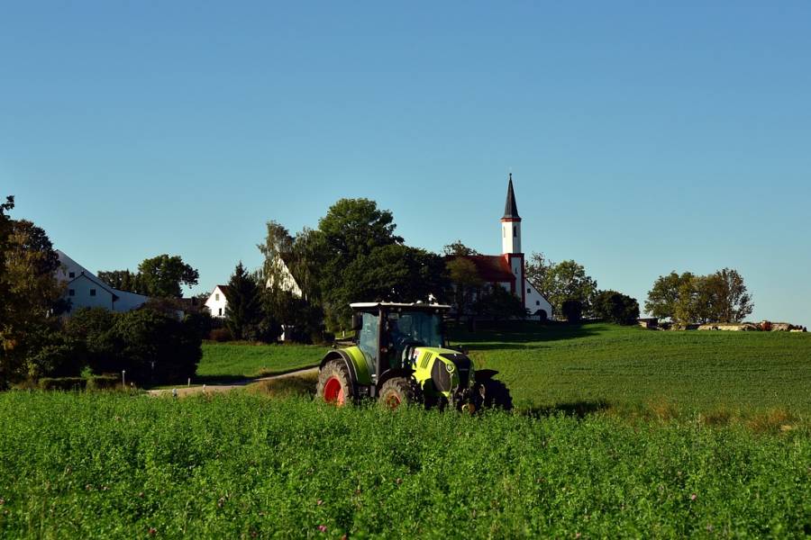 Traktor auf einer Grünfläche vor einem bayerischen Dorf. (Symbolbild: Ulrike Leone)