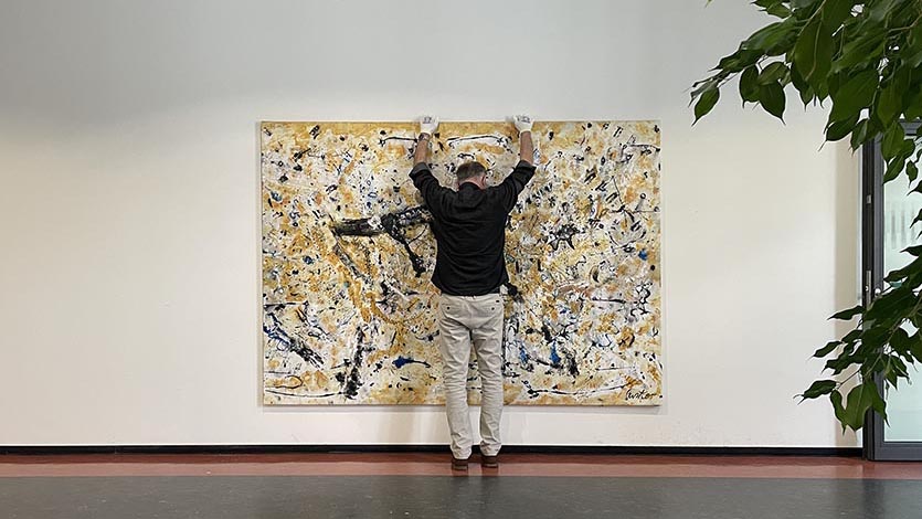 Künstler der Galerie ARTprotect hängt ein großformatiges Kunstwerk an eine Wand - Kunstservice der Galerie ARTprotect Berlin