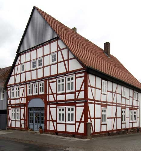 Altes Bauerhaus im Fachwerstil mit braunem Fachwerkständern und weißen Putzfeldern. Zu sehen ist die Giebelseite und eine Dachseite.