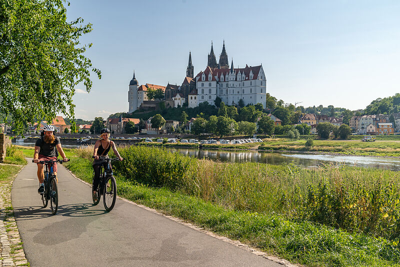 2 Radfahrende auf dem Elberadweg am der Elbe mit Albrechtsburg Meißen im Hintergrund