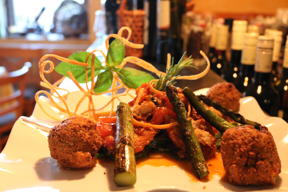 Kalbsrückensteak in einer Kruste von Parmesan, Ei und gerösteten Pinienkernen, angerichtet auf einer Cocktailtomatensauce mit Zucchini und grünem Spargel, serviert mit hausgemachten Gemüsekroketten ( Low-Carb Gericht )