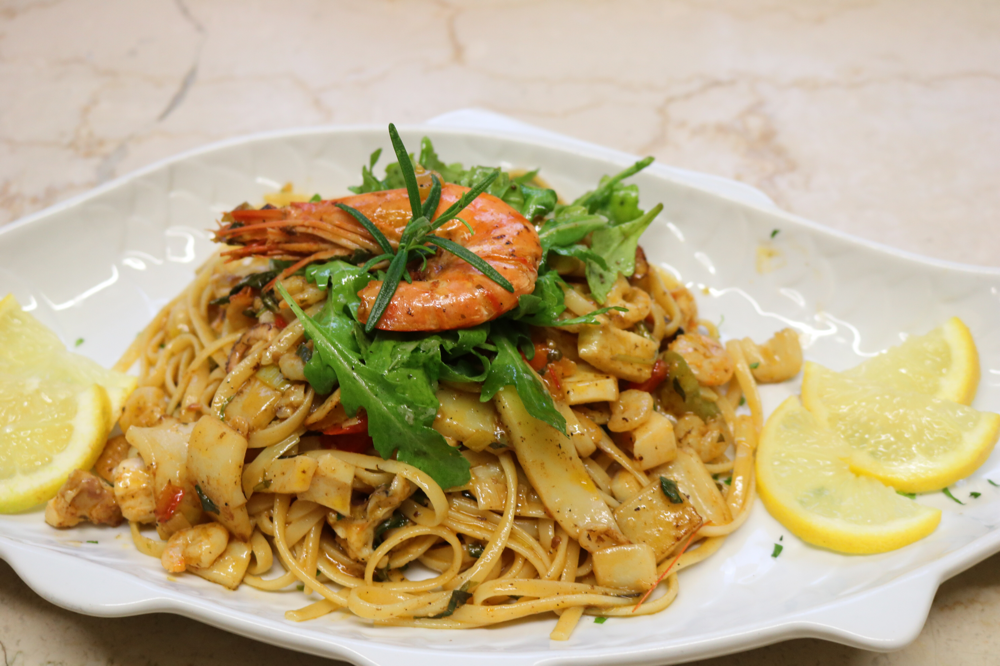 Linguini Marinara mit einem hausgemachten Meeresfrüchtecocktail aus frischem Fisch in leichter Weißweinsauce mit Rucola und Scampi garniert