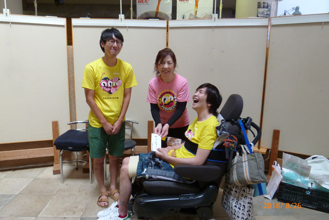 24時間テレビのチャリティTシャツを着て笑う車椅子の男性とその奥で微笑む男性と女性