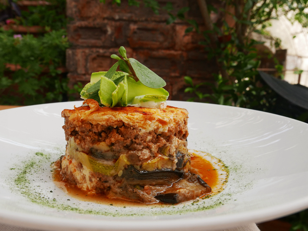 Teller mit einem Stück griechischer Moussaka, Auberginenauflauf mit Hackfleisch, dekoriert mit Kräutern