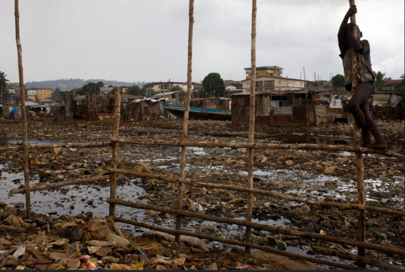 Un bambino vicino a pericolose acque di scolo insieme a zanzare e vermi parassiti nello slum di Kroo Bay a Freetown, in Sierra Leone