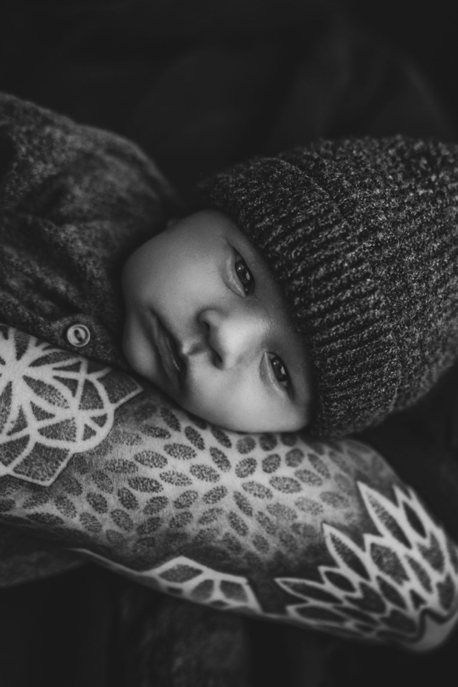 schwarz weiß Foto eines Babys liegend in tättowiertem Arm mit Strickmütze