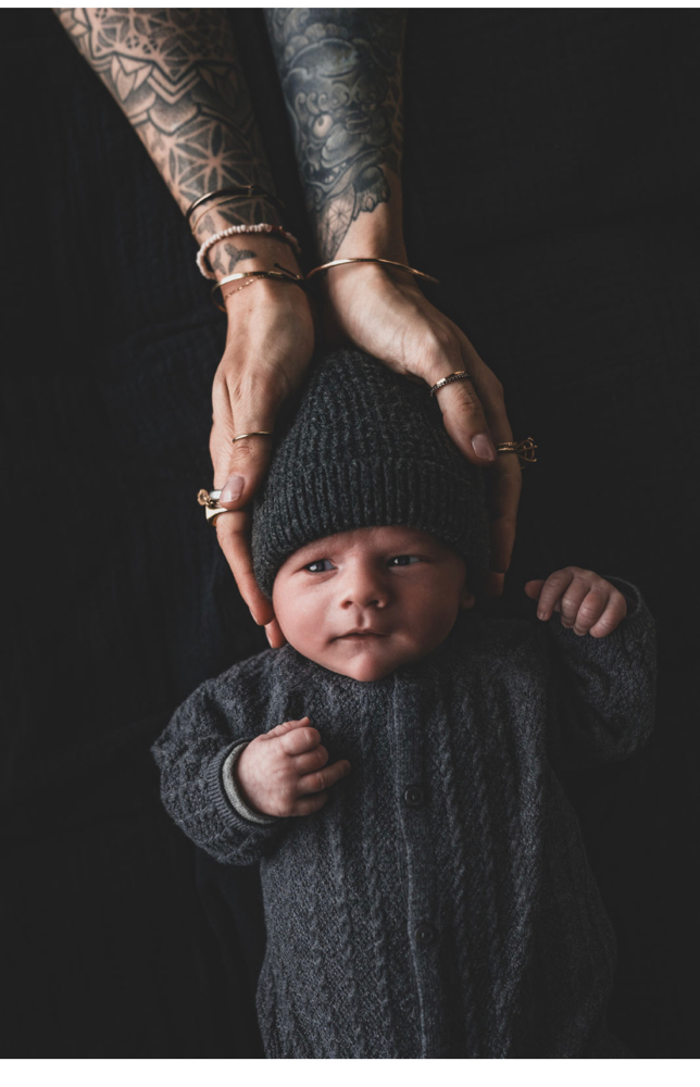 Baby aucf schwarzer Decke, liegend auf Rücken, Hände hakten den Kopf, tättowierte Arme