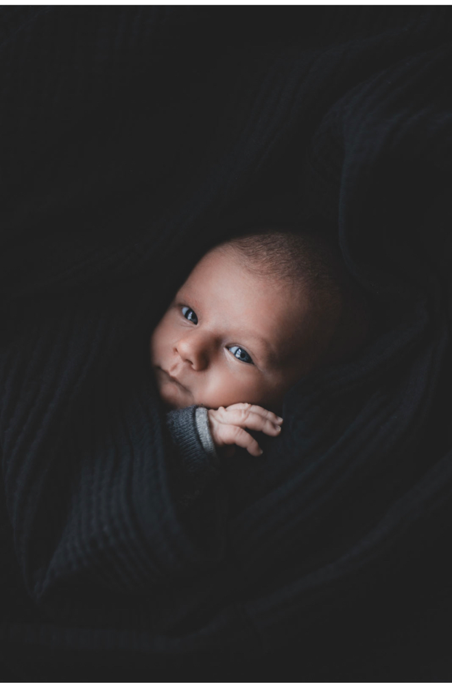 Babyportrait, Baby schaut in Kamera, kleine Hand stützt Gesicht. schwarze Decke