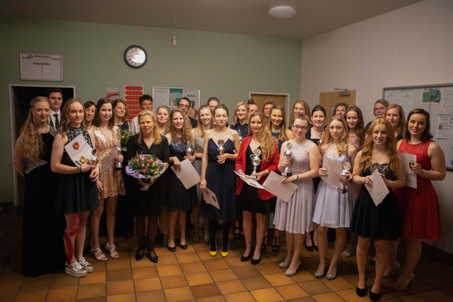 Gruppenbild der Vereinsmeister mit Pokalen und Blumen, Teilnehmerinnen in festlicher Kleidung, lächelnd in einem Saal.