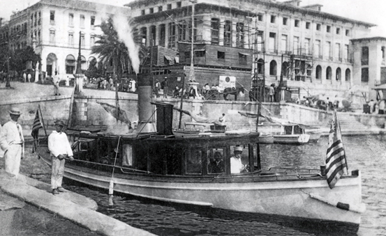 1905 - Customs cutter leaves the dock at the U.S. Custom House in San Juan, Puerto Rico. In the background is the U.S. Post Office then under construction.