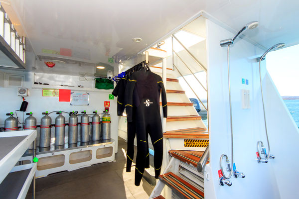 Two wet suits hang to dry, oxygen tanks and showers can also be seen in the photo 