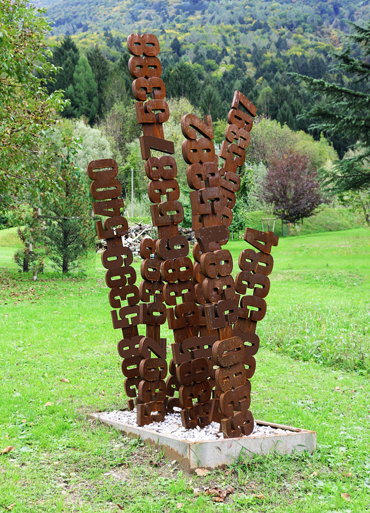 Piera by Paolo Grassi, numerical sculpture installed outdoors with stacked digits forming vertical columns in a natural landscape