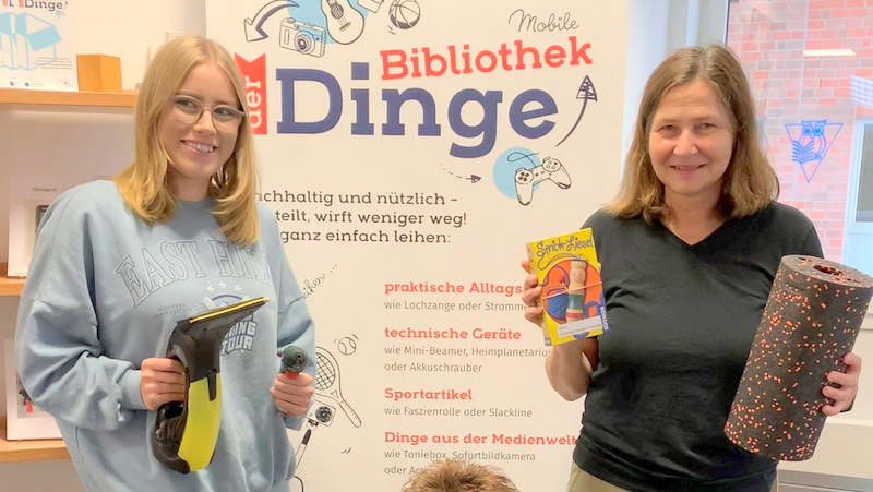 Noelle Griesbach (Auszubildende) und Sabine Treuten (v.l.) präsentieren die Mobile Bibliothek der Dinge in der Stadtbücherei.