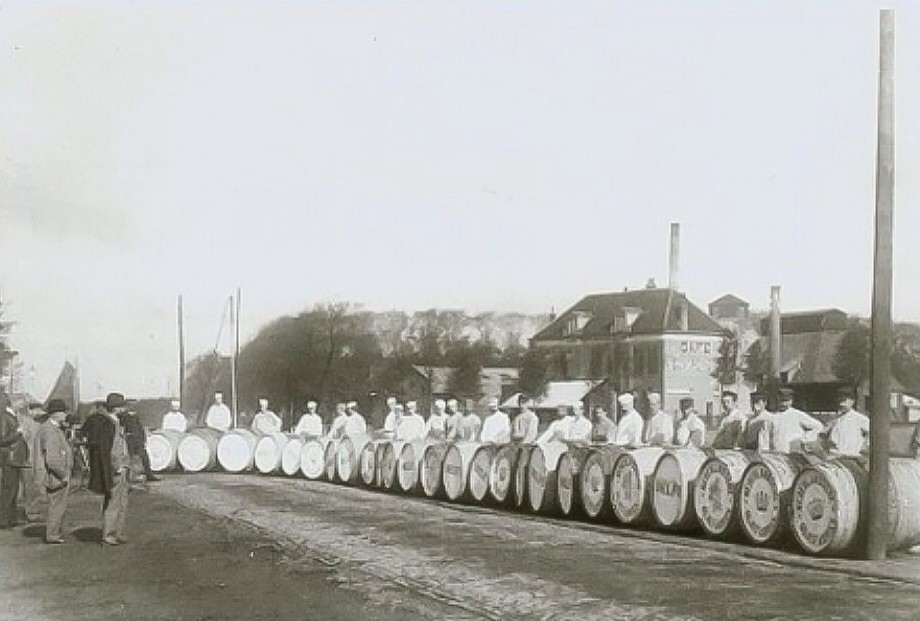Olievaten met personeel in witte pakken op de Wateringseweg vòòr Calvé, gezien naar het noorden. Op de achtergrond café Nieuw Reineveld aan de Haagweg. In 1890 werd dit café verkocht aan de firma Vreede van Rinsum en Co, ijzergieters en machinefabrikanten