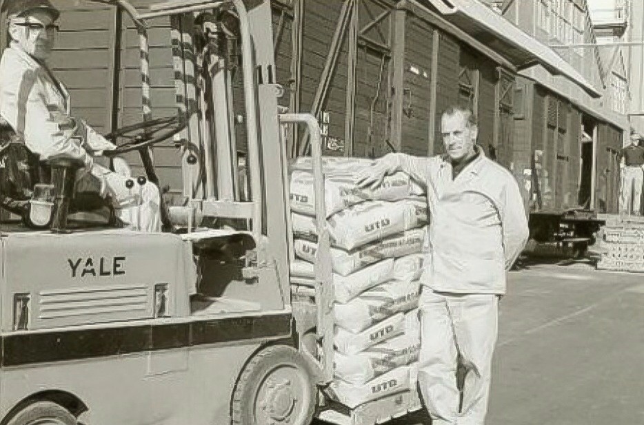 Vorkheftruck met zakken Delfia mengvoeder op het fabrieksterrein van Calvé aan de Wateringseweg. Rechts de heer P. Stigter. 1975