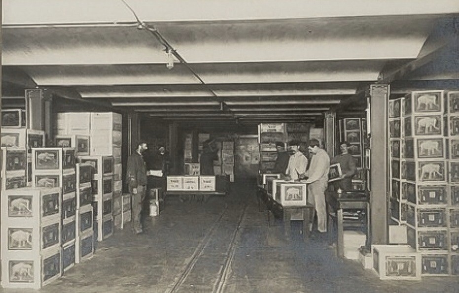 Interieur van het oliemagazijn van Calvé aan de Wateringseweg. Medewerkers van Calvé omringd door kisten met olieflessen. 1900