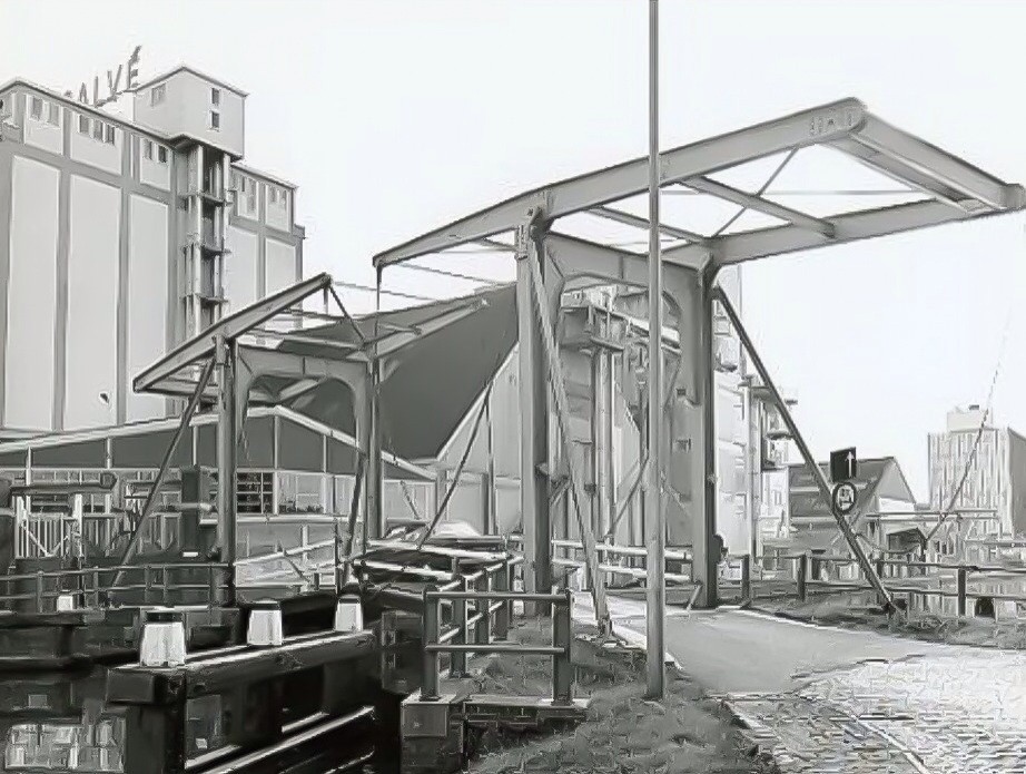 Kolenhavenbrug aan de Wateringseweg gezien naar het zuiden. Links een gedeelte van de silo en rechts de gebouwen van Calvé aan de haven. Meer gebruikelijke, maar onofficiële namen voor de brug zijn Calvébruggetje en Kippebruggetje. Het bruggetje is in 191
