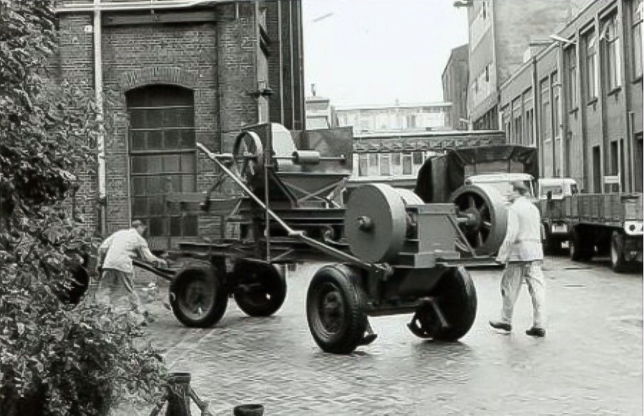 Onbekend voertuig wordt door werknemers verplaatst op het terrein van de Calvéfabrieken aan de Wateringseweg. Op de achtergrond is de hoofdingang te zien.  1970