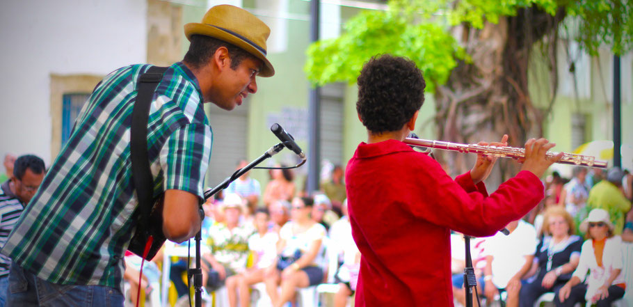 Man spielt Ukulele und Jung spielt die Flöte in einem Open Air Samba Konzert vor einem sitzenden Publikum