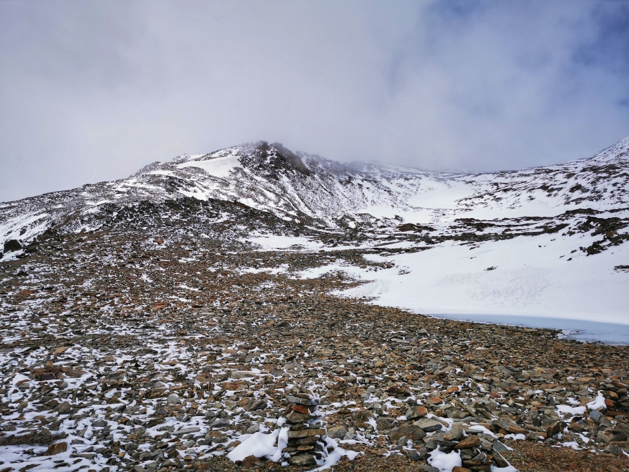 Ein flaches Plateau wird überquert, dahinter schwingt sich der Gipfelaufbau auf, leider in den Wolken