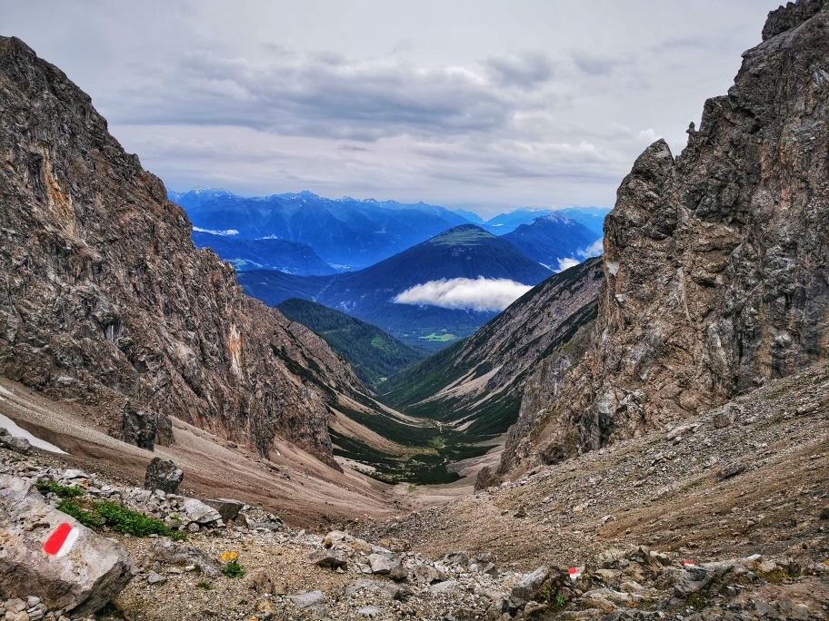 Der Blick ins Tal und den Abstiegsweg, im Hintergrund die schneebedeckten 3.000er des Sellrain