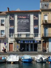 Façade du musée des arts modestes à Sète au bord du canal du centre, avec trois bateaux à quai, cet ancien chai à vin est parfaitement intégré à la rangée des maisons.