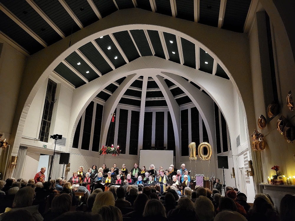 Die Chormitglieder stehen im Mittelgang der Kirche und winken und lächeln in die Kamera.