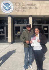 Picture of Claudia and her husband standing in from of the U.S. Immigration Services building and posing with her naturalization certificate.