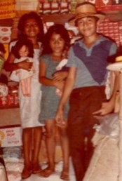 Claudia in the middle with her older brother on the left and her sister on the right standing together in a shop in El Salvador.