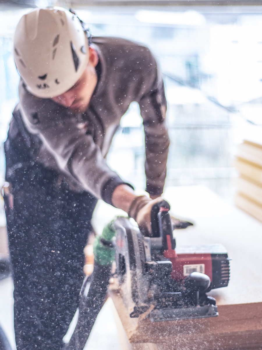 fotografie bau handwerker arbeitet mit der hobelmaschine und es fliegen spaehne