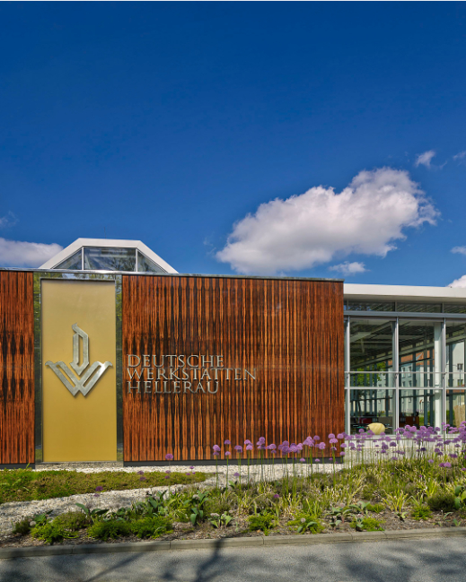 Eingangsbereich der Deutschen Werkstätten Hellerau mit blauem Himmel und DWH Logo an der Fassade