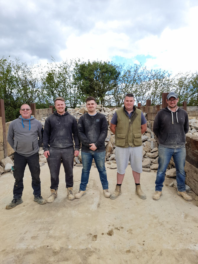 Five men lined up in front of stone